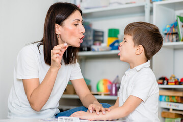 Obraz na płótnie Canvas Beautiful woman speech therapist teaches boy the correct pronunciation of words and sounds in the office