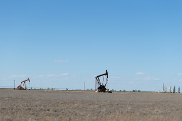 Oil drilling well rig in Texas in late afternoon heat waves on a windy day in a field with shallow depth of field and selective focus on one pump