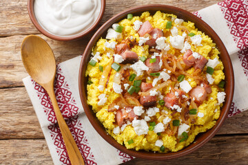 Corn porridge served with cheese, fried onion and bacon closeup on the bowl on the wooden table. Horizontal top view from above