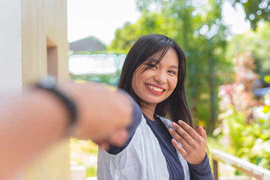 A pretty lady wearing a cardigan and navy blue long sleeves top is reaching out her hand while smiling widely. A blurry hand is shown in the picture.