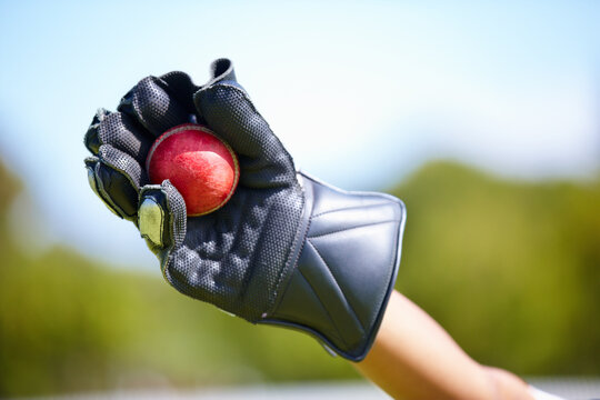 Cricket, ball and hand with a wicket keeper making a catch during a sports game outdoor on a pitch. Fitness, glove and caught with a sport player playing a competitive match outside during summer - Powered by Adobe