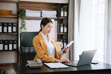 Young beautiful woman typing on tablet and laptop while sitting at the working wooden table office.