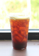 A cup of iced coffee sits on a window sill.