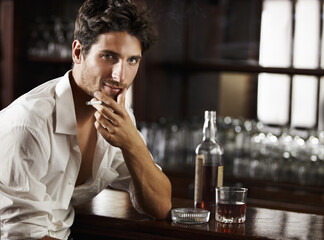 Portrait, whiskey and smoking or young man or tobacco on counter and cigarette on bokeh. Sexy, masculine and male model with glass or ash tray or handsome guy relaxing with drink and smoke after work