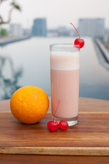 Close Up Mixed Smoothies. Orange and Strawberry is the ingredients. Served with ice and cherry sliced on the top of glass. Pool view. This smoothies suitable for summer drink