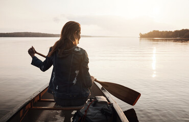 Paddling along the calm waters. Rearview shot of a young woman enjoying a canoe ride at the lake. - obrazy, fototapety, plakaty
