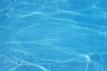 Blue water with ripples on the surface. Defocus blurred transparent blue colored clear calm water surface texture with splashes and bubbles. Water waves with shining pattern texture background.