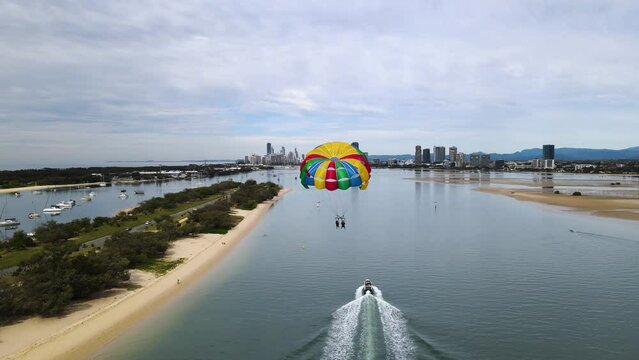 Colourful parasailing along a popular coastal holiday town with an urban city skyline background. Drone view