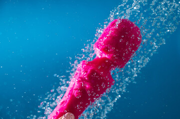 A woman washes a pink vibrator under running water on a blue background. Sex toy hygiene concept.