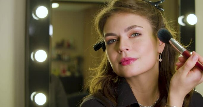 Close-up video of a young Caucasian woman applying makeup in fromt of mirror at home.