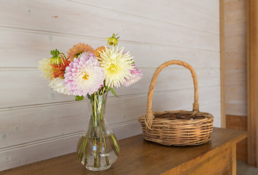 Close up of colorful dahlia flowers in glass vase on table with wicker basket in background (selective focus)
