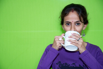 A smart and cute girl drinking coffee, a coffee cup grabs with both hands against a green screen....
