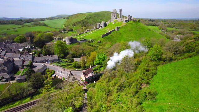 Aerial shot of steam train passing in front of Corfe Castle on a summer day