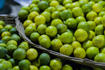 Lemons and limes of green and yellow color are kept in bulk inside a basket or tray made of cane in a market for selling. Great source of vitamin c.