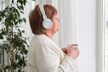 Elderly lady with headphones, enjoying coffee and a smile - serenity and happiness. Retirement bliss: joyful elderly lady sips coffee listens to music contentment