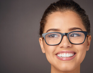 Looking at the beautiful side of life. Studio shot of a beautiful young woman wearing glasses against a gray background.