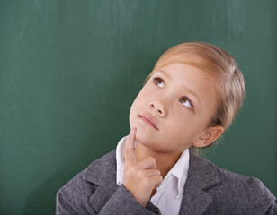 Thinking about her schoolwork. A young schoolgirl looking thoughtful in front of the greenboard.