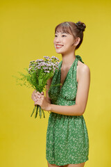 pleased cute lady with gentle toothy smile, dressed in fashionable dress, holds flowers closely to herself
