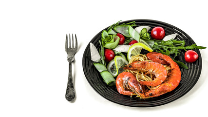 Fried shrimp with spaghetti and fresh vegetables on a black plate isolated on a white background.