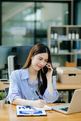 Business asian woman Talking on the phone and using a laptop with a smile while sitting at office.