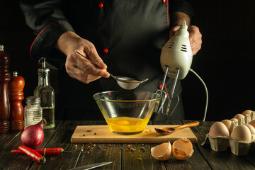 The chef prepares a delicious eggs omelette for breakfast. The cook uses an electric mixer in the restaurant kitchen for cooking