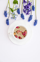 Healthy herbal tea in a white cup with medicinal herbs, spring flowers and Chinese tea rose buds Mei Gui Hua for relaxation and wellness. Floral Infusion, top view, vertical