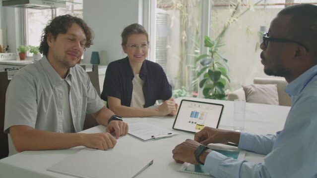 Family couple shaking hands and speaking with African American sales representative on office meeting while going to buy solar-powered home