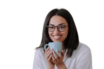 Adorable african american female in glasses and white t-shirt holding cup of coffee, sits against transparent background on sofa looks at camera, broad smiling. Brazilian young woman enjoys holidays.
