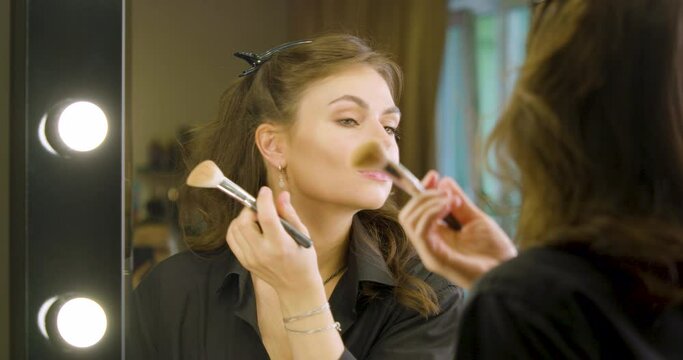 Sensual Caucasian woman applying makeup in fromt of mirror.