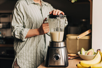 Woman blending spinach, berries, bananas and almond milk to make a healthy green smoothie