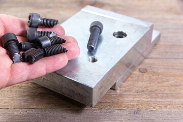 Broken black bolts in worker's hand. Screw threading in a steel billet on a wooden board. Bolt with...
