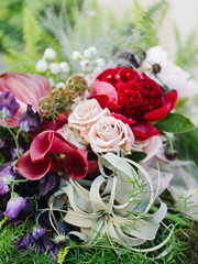 Bright exotic bouquet of tillandsia, pink roses, red callas, red peony, irises, flowers close-up. The bride's bouquet.