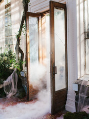Fog rolls in from the open wooden doors of the greenhouse. Smoke spreads across the floor.