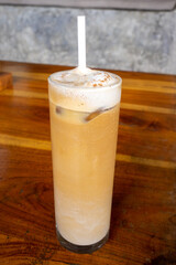 A glass of iced latte on a brown wooden table in a cafe. Close up on a narrow glass with a refreshing cold coffee with a straw.