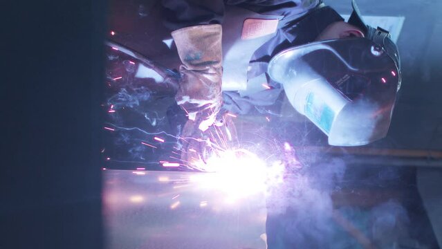 Vertical shoot. Asian welder solder iron. Man at workshop surrounded by tools. Worker dressed in special apron and safety gloves. Male lifts up protective masc. Employee at workshop.