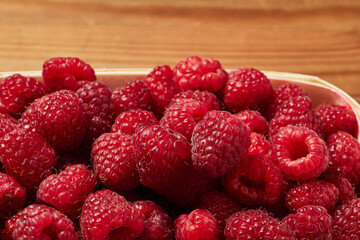 delicious fresh raw red raspberries in natural eco-friendly packaging in a basket of peeled hardwood veneer on a wooden table closeup. harvest. healthy food. diet. summer. vitamins