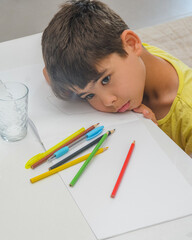 The boy is tired of studying. The child got tired and lay down on the textbook. The boy is engaged in creativity and thinks what to draw, The boy is looking for an idea for drawing. Child at the table