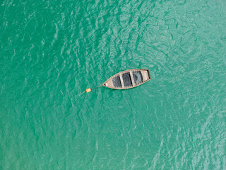 A breathtaking top view of a serene blue-green lake with a wooden boat gently floating on its surface. © Vadim