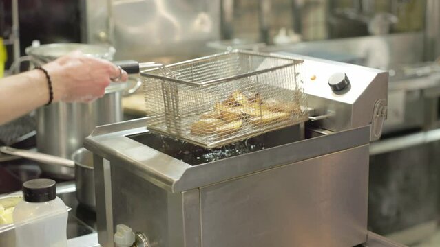 Shaking the basket with french-fries above the cooking oil. Placing the container with french-fries into the boiling cooking oil. French-fries are quickly cooked in the hot oil. Fast Food. Deep fryer