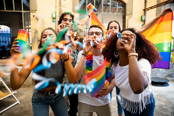 Group of friends celebrate pride with flags and streamers by dancing at a demonstration for support for equality - People having fun together - 599536221