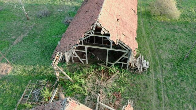 Decaying outbuilding with red roof tiles against green grass in the background