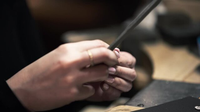 Shot of a female metalworker filing and sanding a silver metal necklace. Shot in a jewellers on the Isle of Lewis, part of the Outer Hebrides of Scotland.