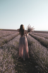 Long-haired slender girl in summer with a bouquet of flowers in a lavender field . Vertical image.