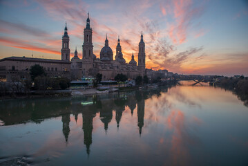Fototapeta na wymiar del Pilar basilica, one of the important architectural symbols of zaragoza, and the Ebro river and its reflection with sunset colors and clouds