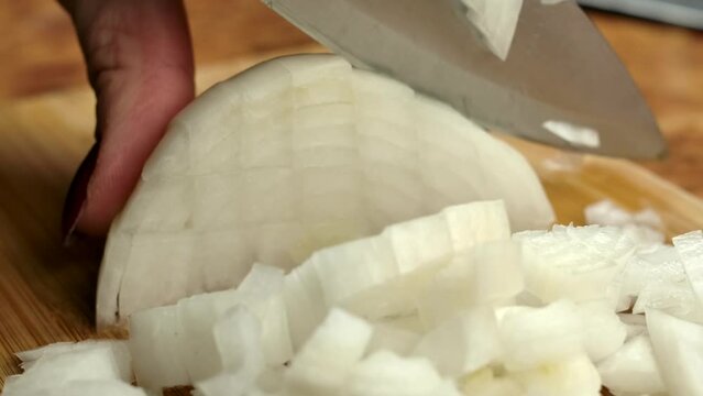 The knife cuts the onion into small square pieces