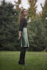 Outdoor portrait of woman in green silk satin skirt and brown blouse in the park during autumn season
