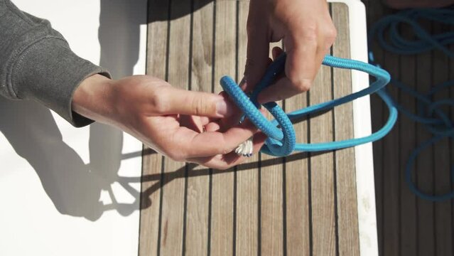 Sailor shows how to tie a bowline knot. Close-up of hands and knot. Top view. Popular knot for mooring. Blue knot. 4К