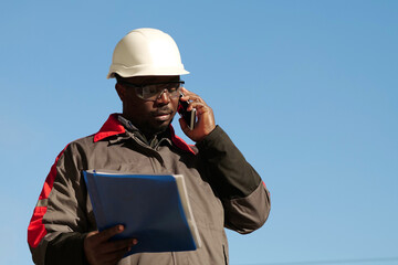 African american builder with work papers talks on smartphone