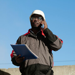 African american builder with work papers talks on smartphone