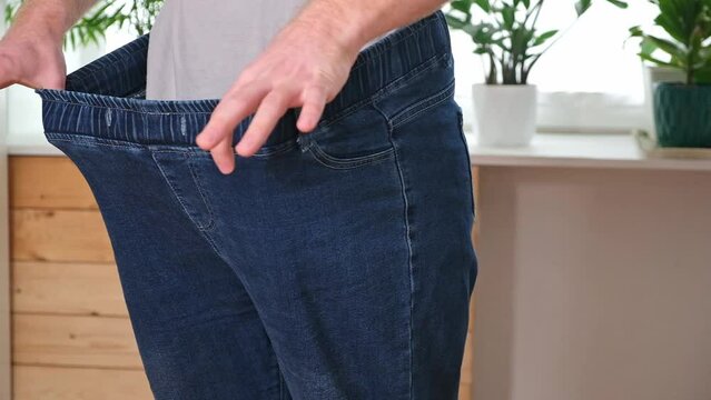 The guy is trying on big jeans after losing weight. Man in oversized pants in weight loss concept
